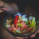 A vibrant bowl of healthy pasta salad with fresh vegetables in a casual setting.
